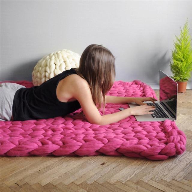 Woman lying on the floor using a laptop under a knit throw blanket