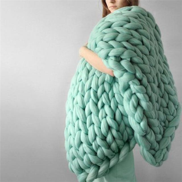 Person wrapped in a knit throw blanket standing against a neutral background