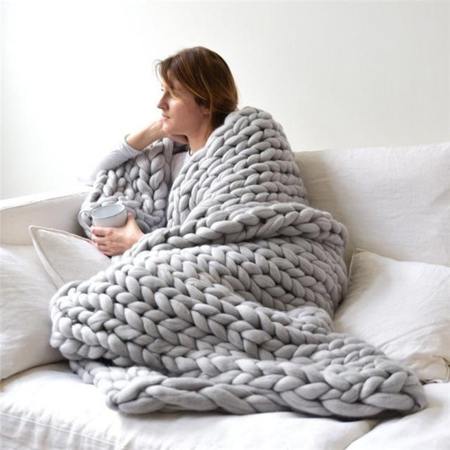 Woman seated on a sofa wrapped in a knit throw blanket holding a cup