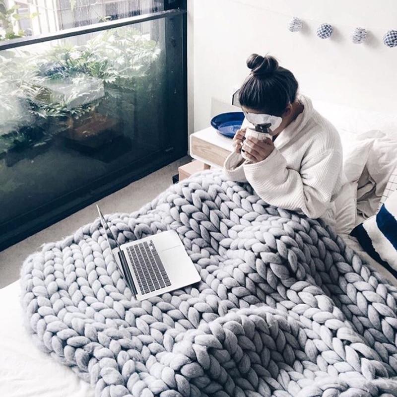 Person using a laptop under a large knit throw blanket on a sofa