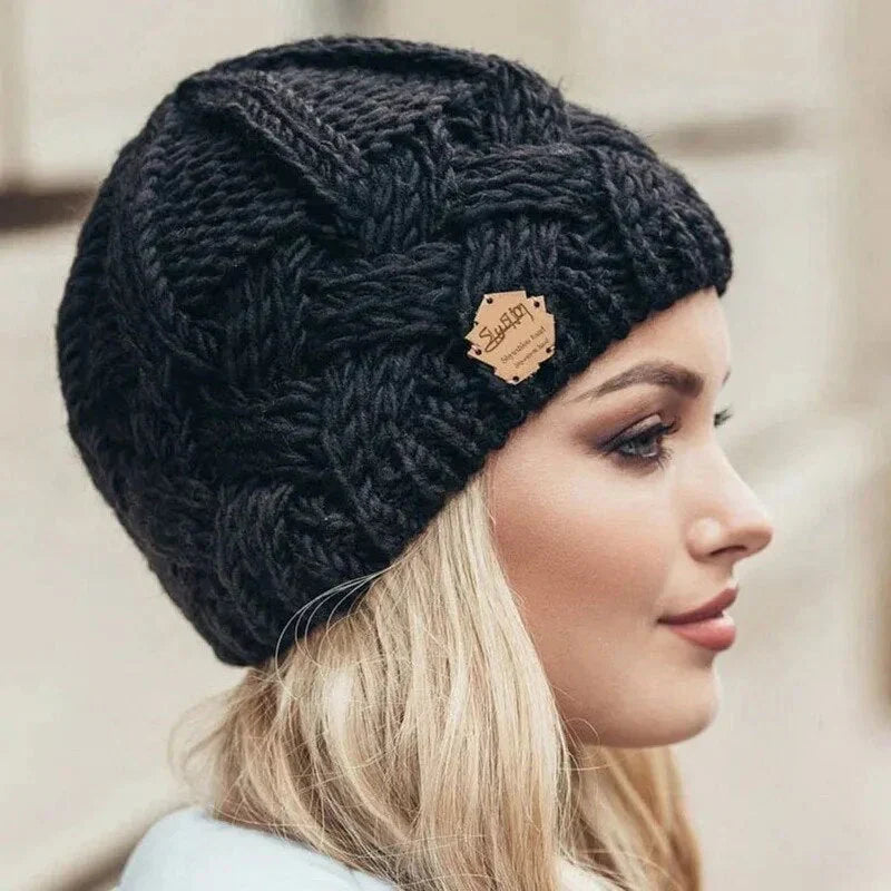 Black chunky knit beanie with braided cable pattern and small logo patch.