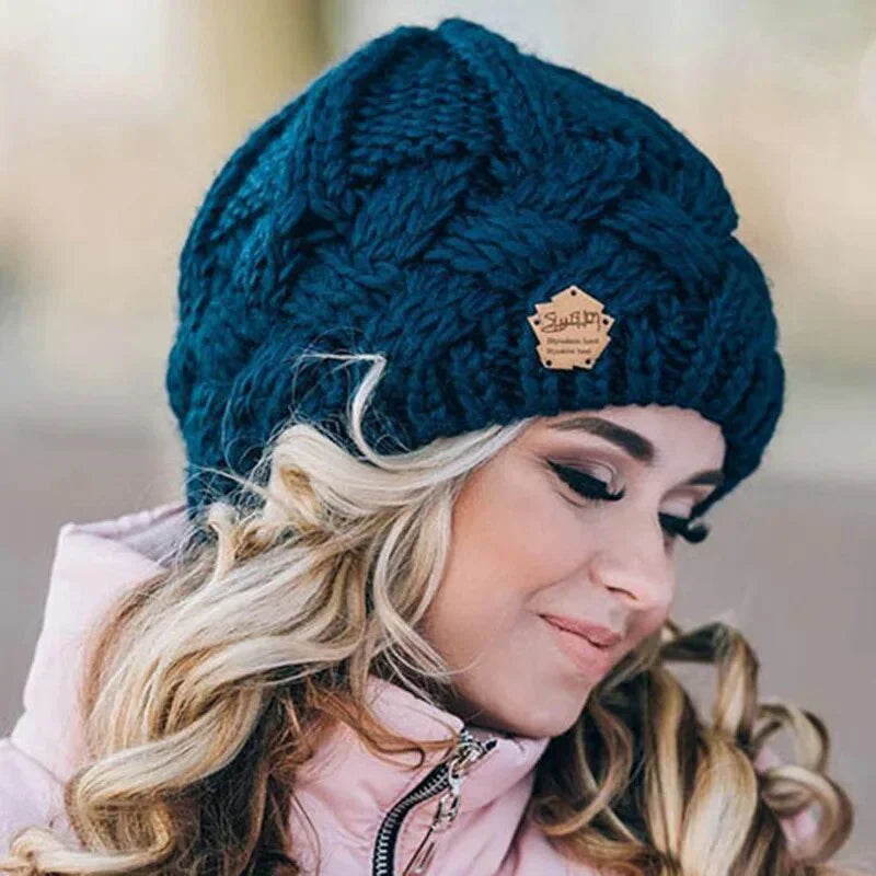 Dark teal chunky knit beanie with raised cable pattern and stitched logo patch.