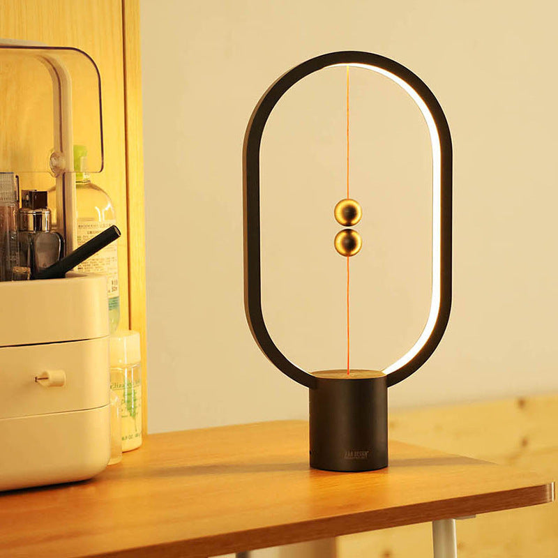 Minimalist oval LED table lamp with warm light and hanging sphere detail.